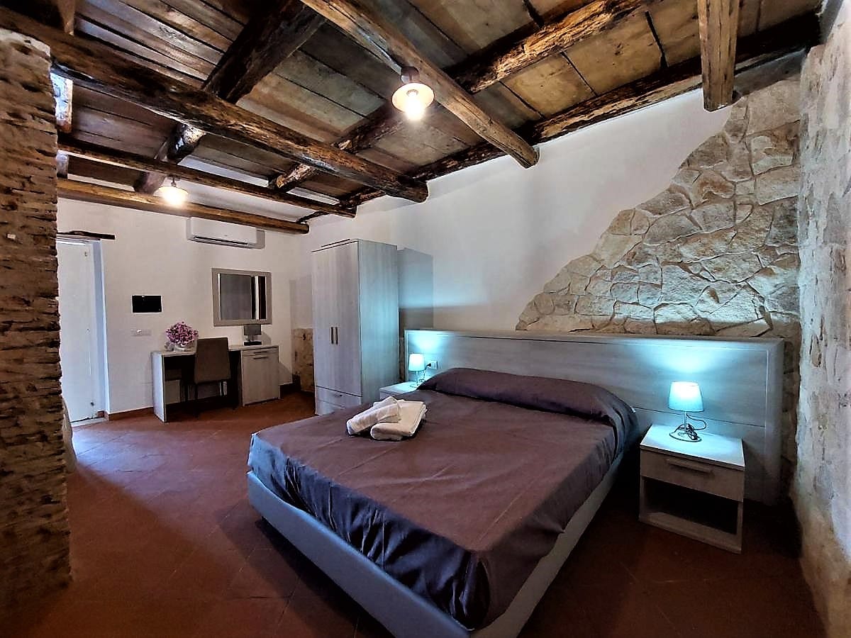 Camera con letto matrimoniale, travi in legno e parete in pietra